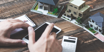 Des maquettes de maisons, une calculatrice, un bloc note, un téléphone et des mains