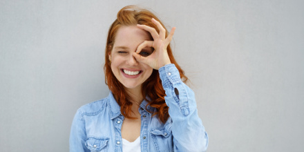 Une femme avec un grand sourire et faisant un monocle avec ses doigts