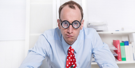 Un homme en chemise cravate avec de grosses lunettes regarde l'objectif d'un air dubitatif
